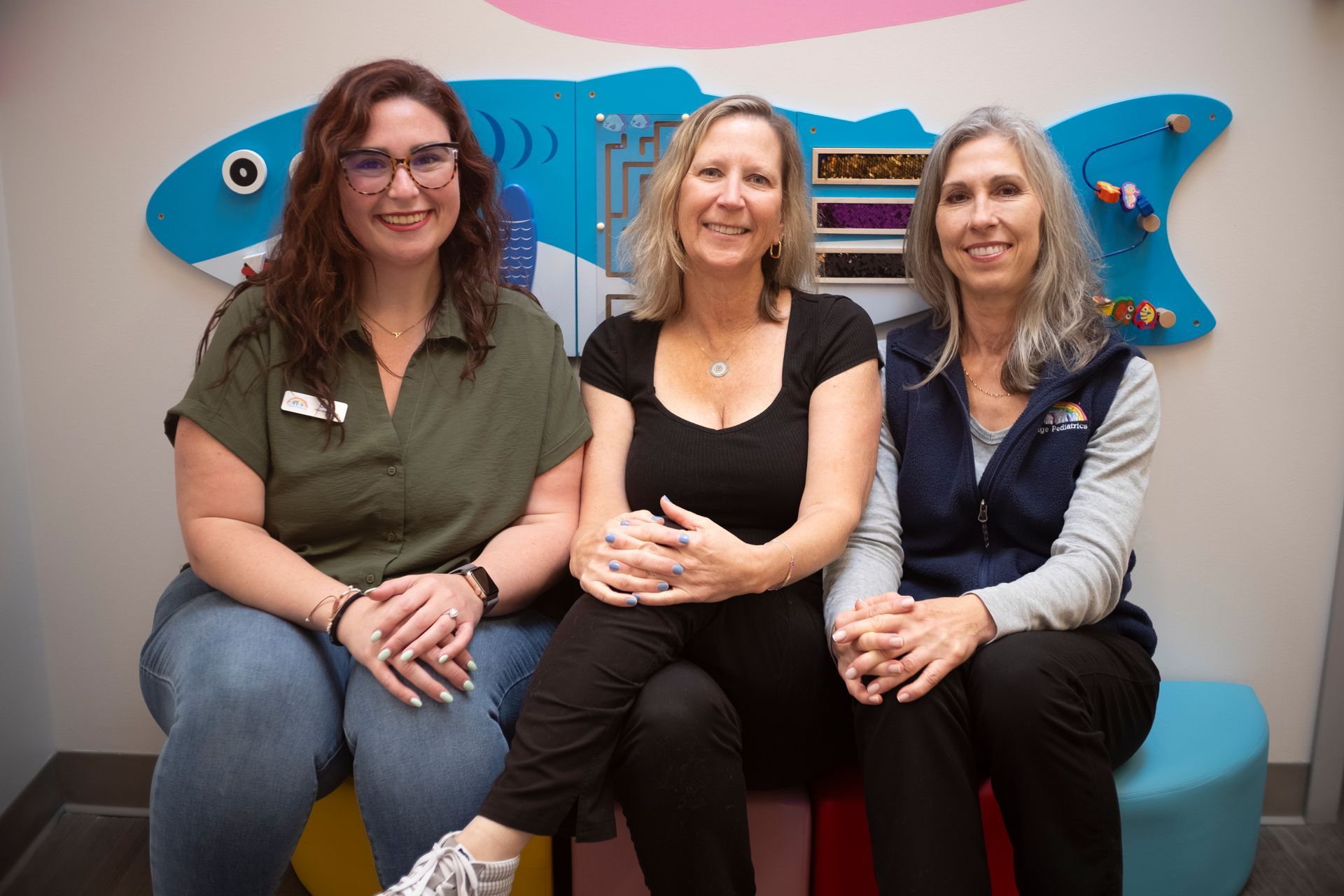 Three women are sitting on a bench in front of a fish mural.