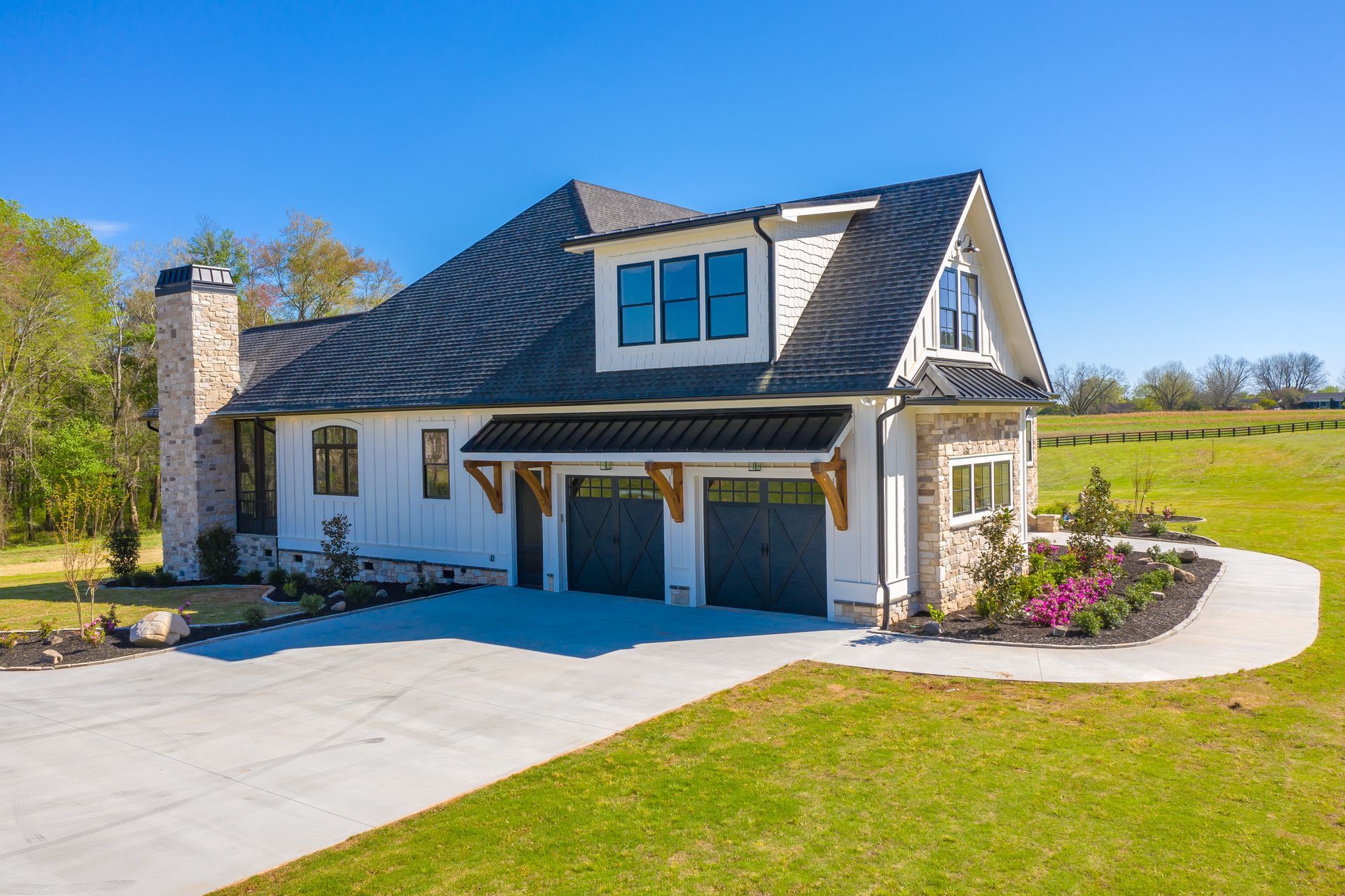 A large white house with a black roof is sitting on top of a lush green field.