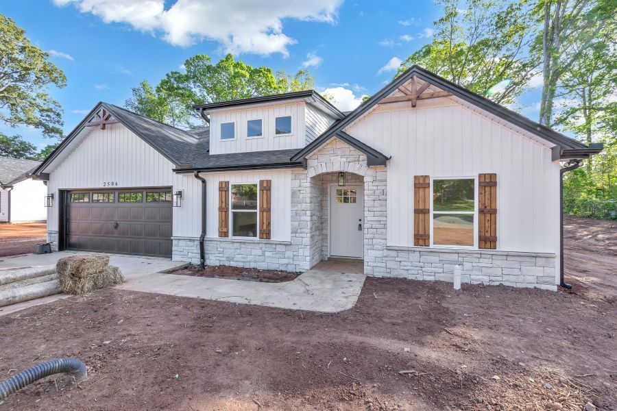 A white house with a black garage door is sitting on top of a dirt field.