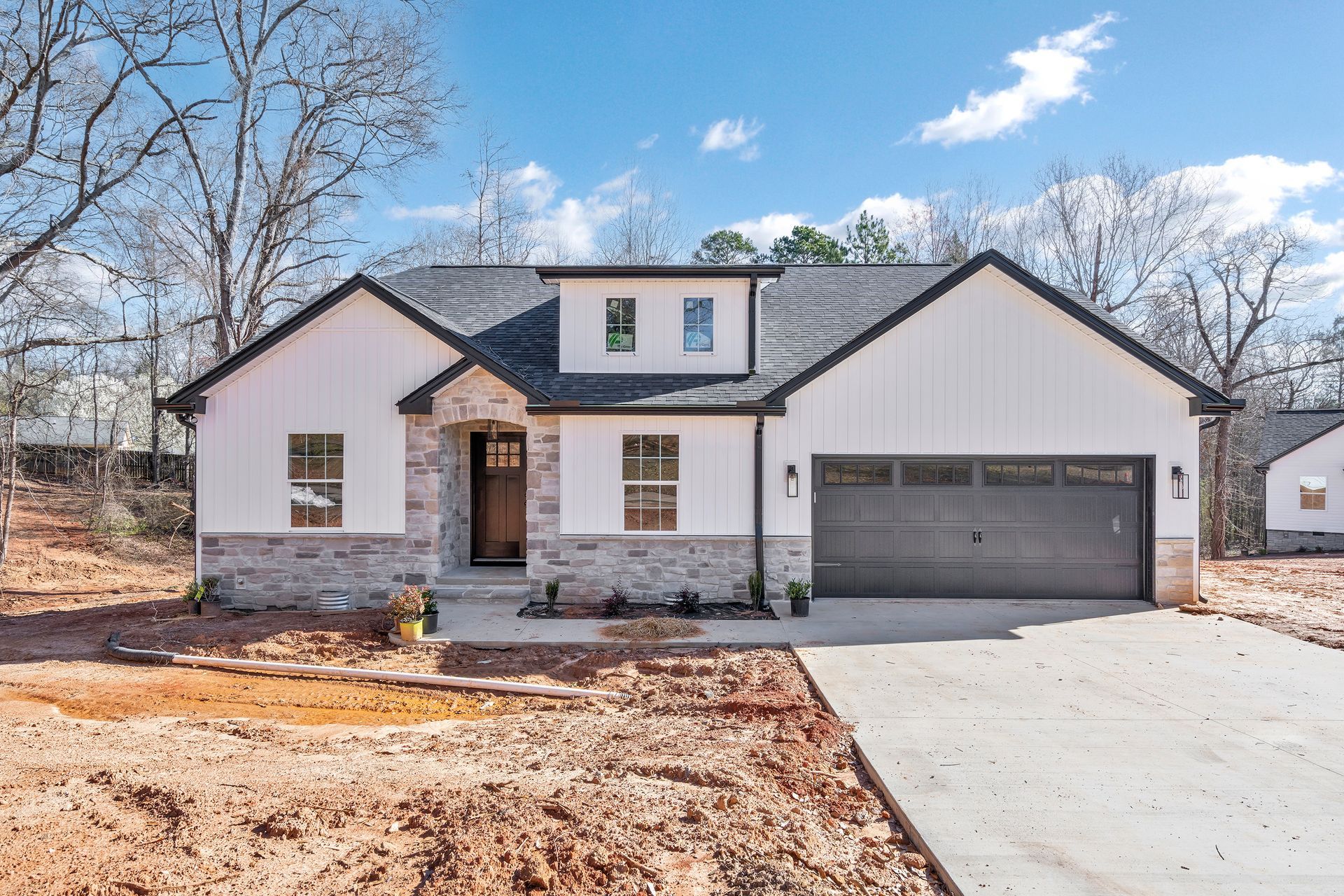A white house with a black garage door is sitting on top of a dirt field.