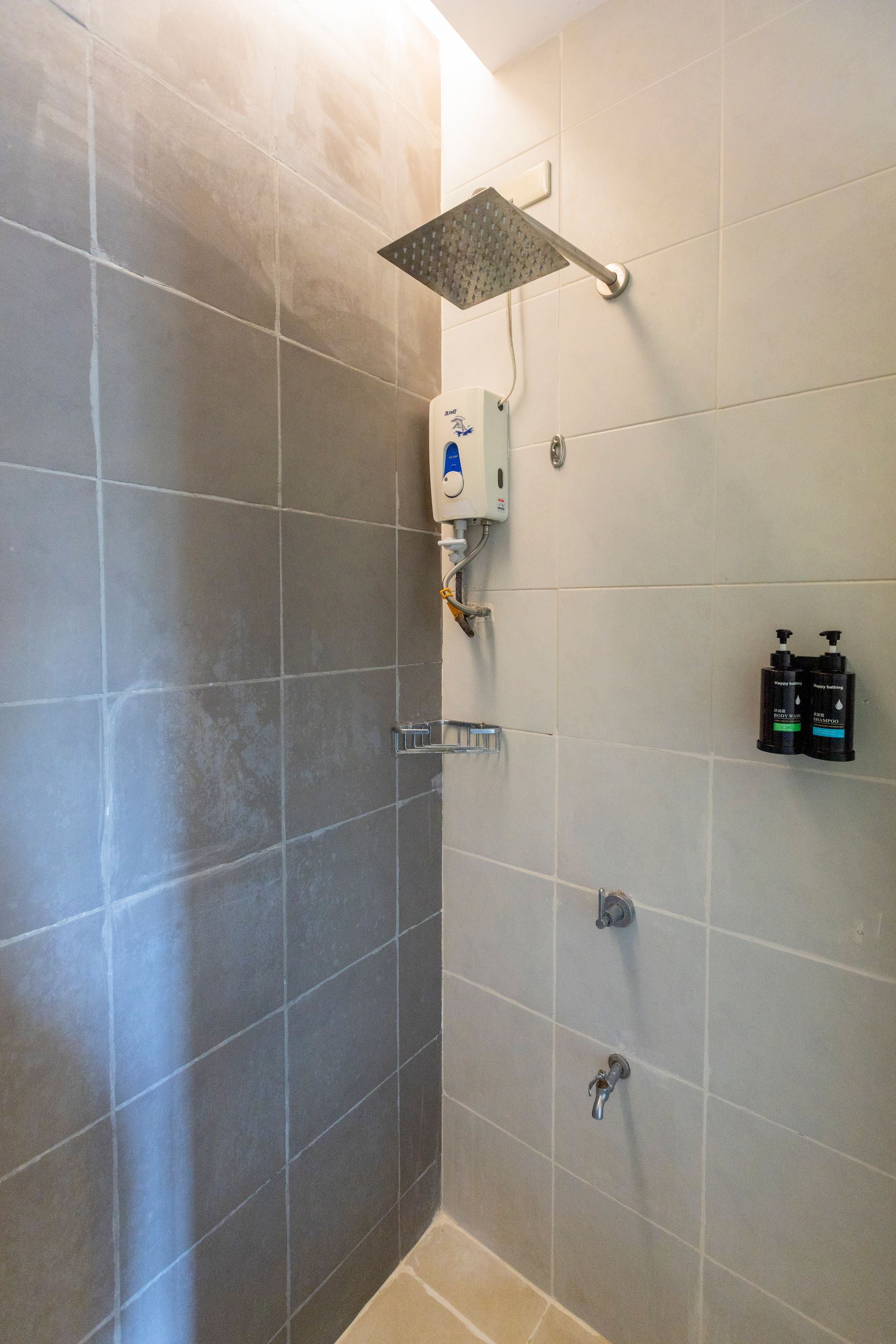 Shower with gray tiled walls, rain showerhead, water heater, and toiletries.