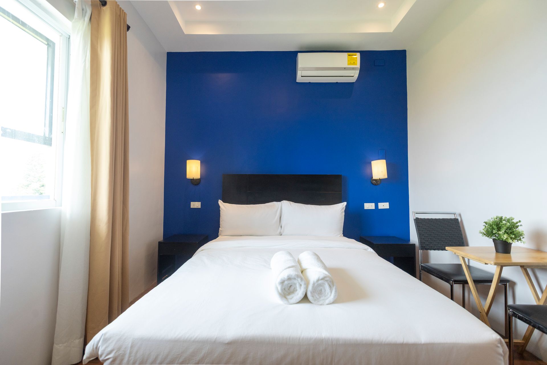 Bedroom with blue accent wall, double bed, small table, and window.