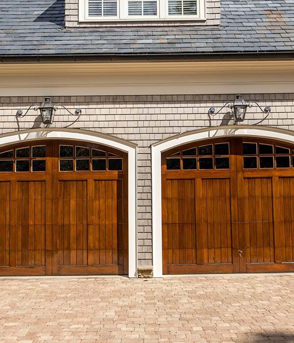 Two wooden garage doors on a beige brick house with arched windows and a stone driveway