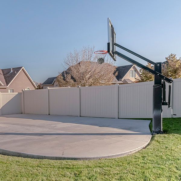 Backyard basketball hoop beside a concrete court and fence on a sunny day