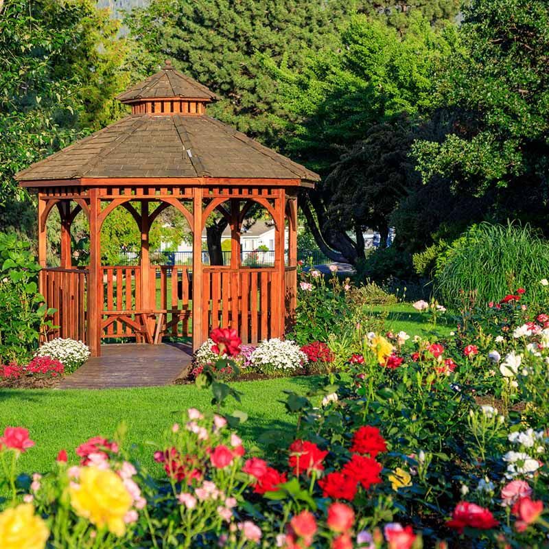 Wooden gazebo in a colorful flower garden with green trees in the background