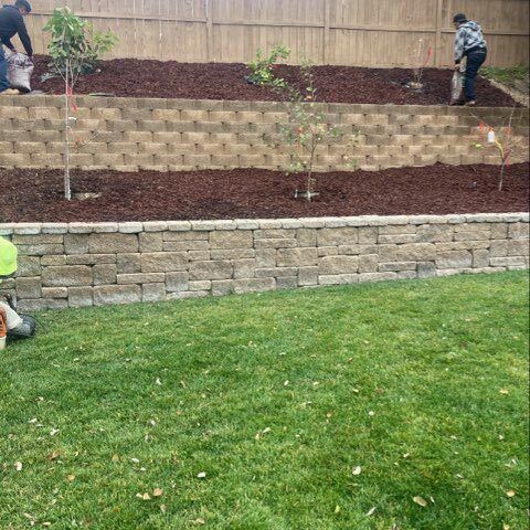 Workers building a tiered backyard retaining wall behind a green lawn.