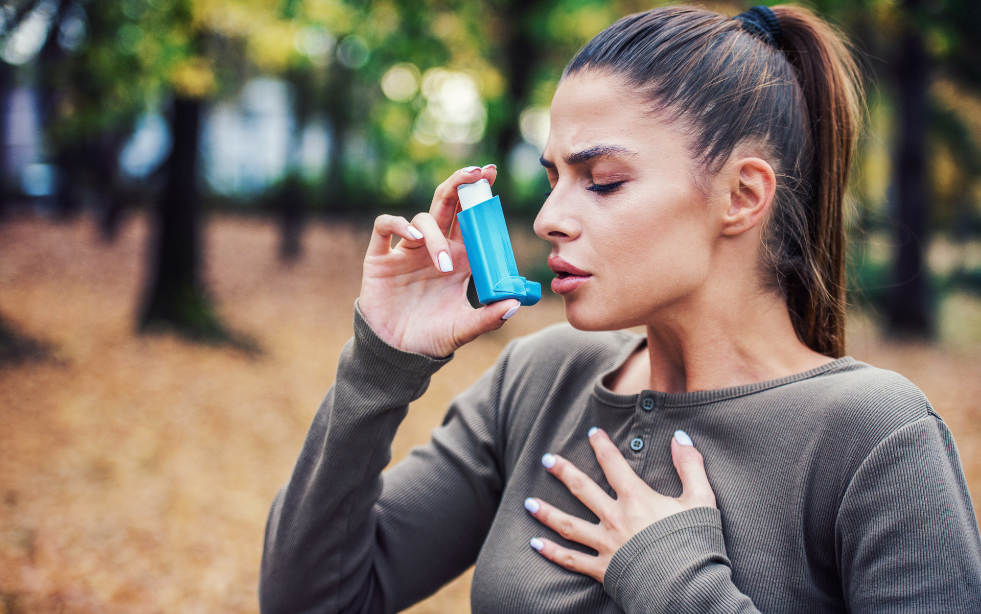 A woman is using an inhaler in a park.