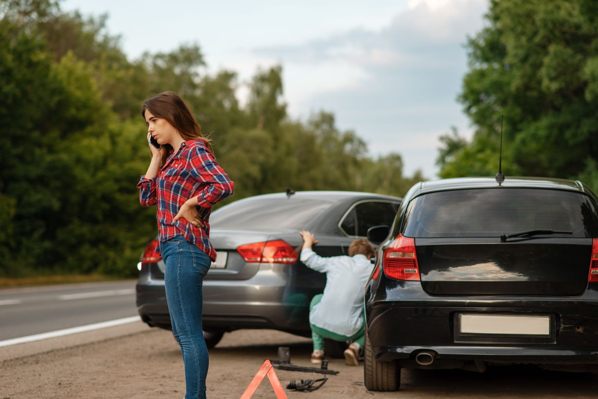 Woman on the phone after an auto accident while a man checks the damage Woman on the phone after an auto accident while a man checks the damage