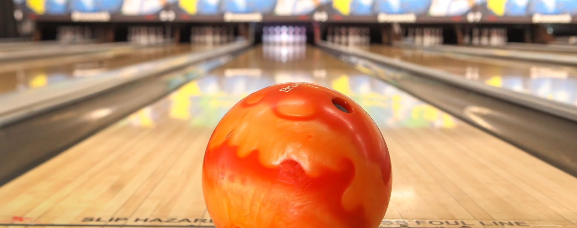 Orange bowling ball on a lane, centered toward the pins in the background