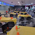 Bowling alley lounge with yellow-covered tables, orange cones, and monitors along the lanes