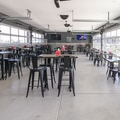 Spacious garage-style bar with high tables, stools, and ceiling fans in a bright, open room