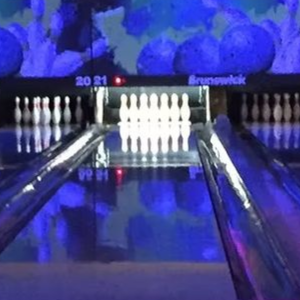 Bowling alley with glowing purple and blue lane lights, viewed from behind a seated bowler.