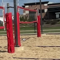 Outdoor beach volleyball court with red net posts and a red “BEACHES PUB” sign in the background
