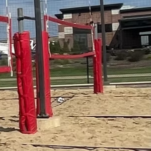 Outdoor beach volleyball court with red net posts and a red “BEACHES PUB” sign in the background