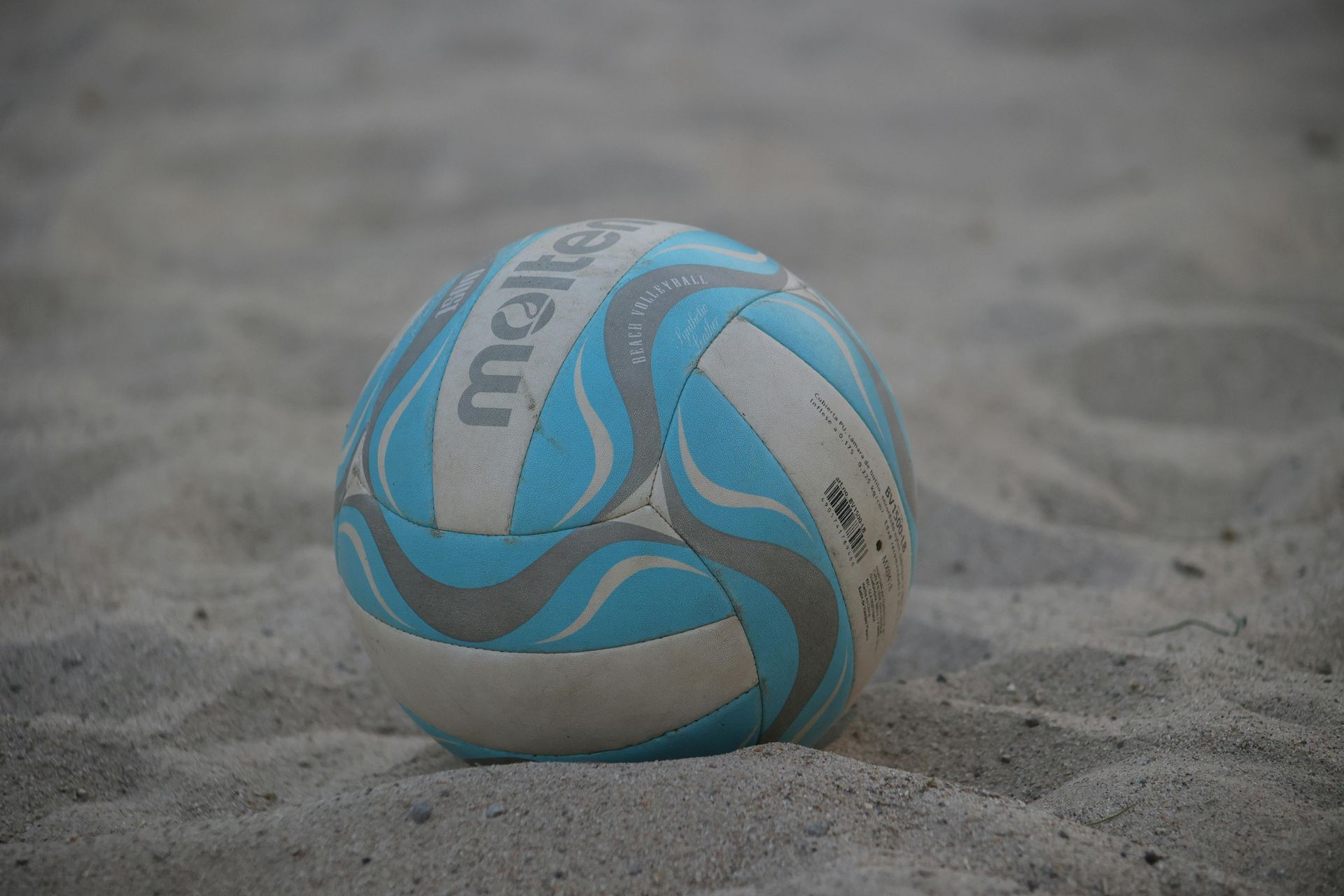 Blue-and-white volleyball resting on sandy beach sand