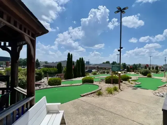 Mini golf course with bright green putting greens, landscaping, and a clear blue sky