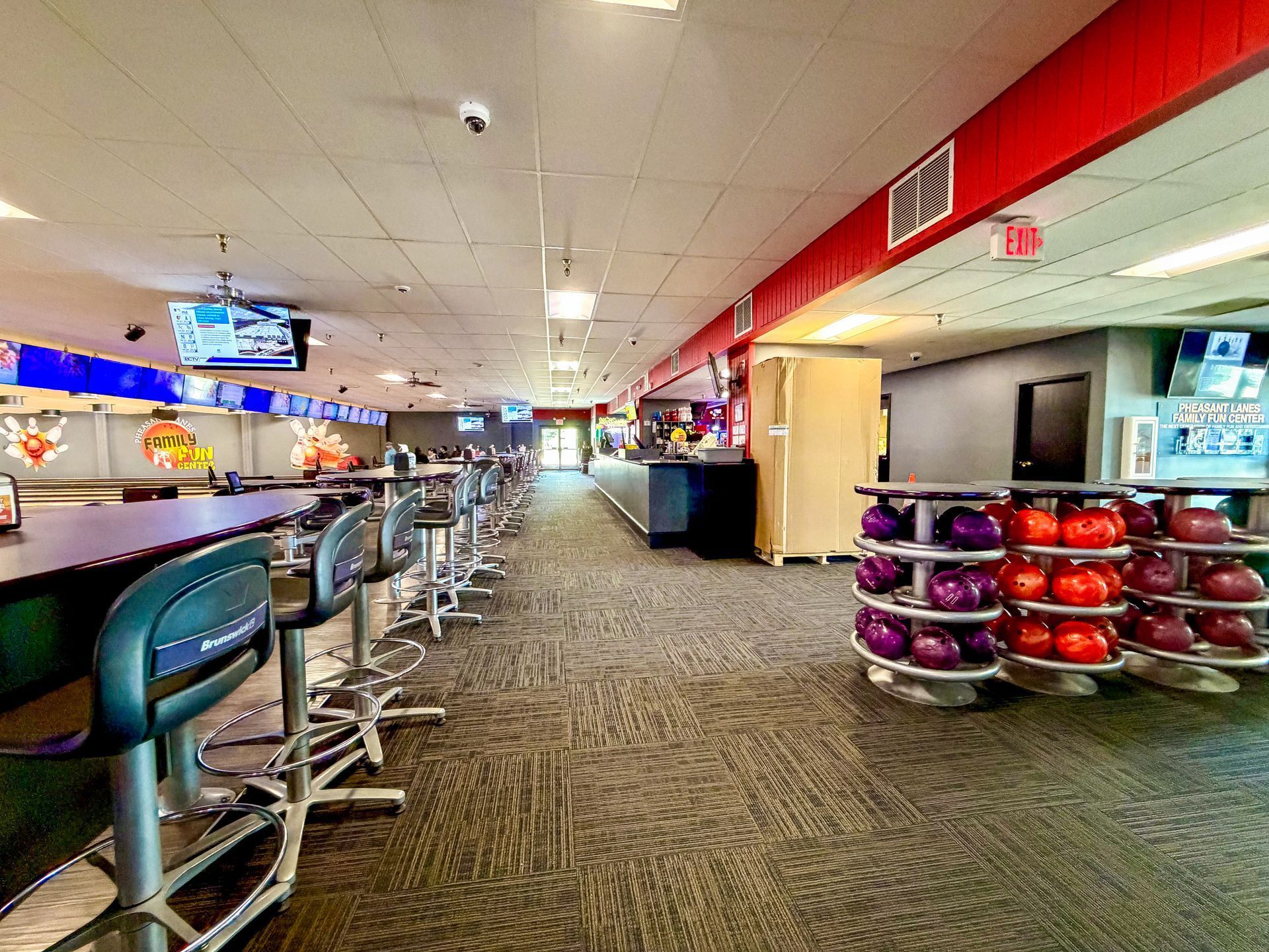Person reaching for a bowling ball in a bowling alley, with colorful balls in the foreground.
