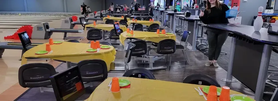 Bright cafeteria with round yellow tables, black chairs, and colorful centerpieces under hanging decor
