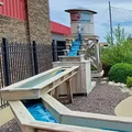 Mini golf hole with a tunnel, landscaped rocks, shrubs, and a water feature under a cloudy sky