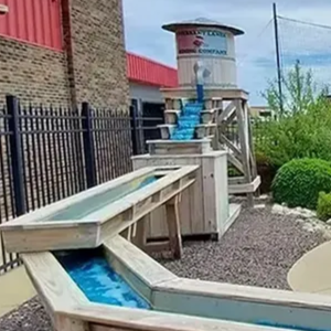 Mini golf hole with a tunnel, landscaped rocks, shrubs, and a water feature under a cloudy sky
