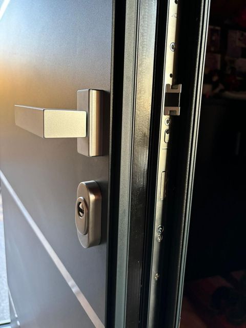 Primo piano di una maniglia e di una serratura argentate su una porta nera parzialmente aperta.