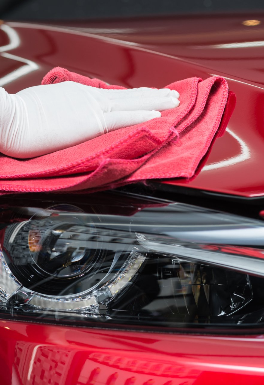 A person is cleaning a red car with a towel and gloves.