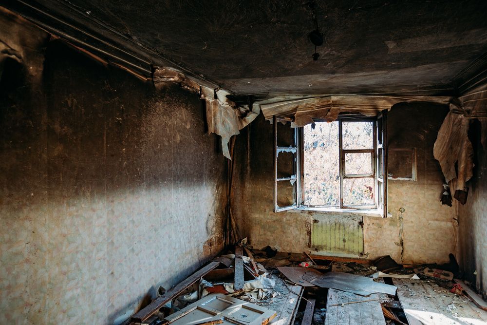 An empty room with a window and a lot of trash on the floor.