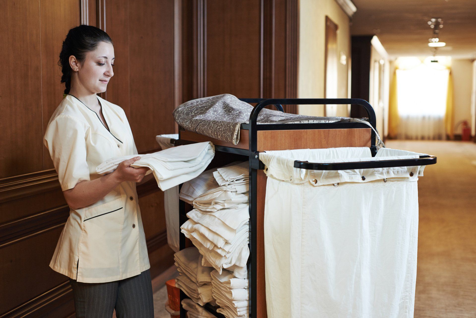 A maid is standing next to a cart full of towels.