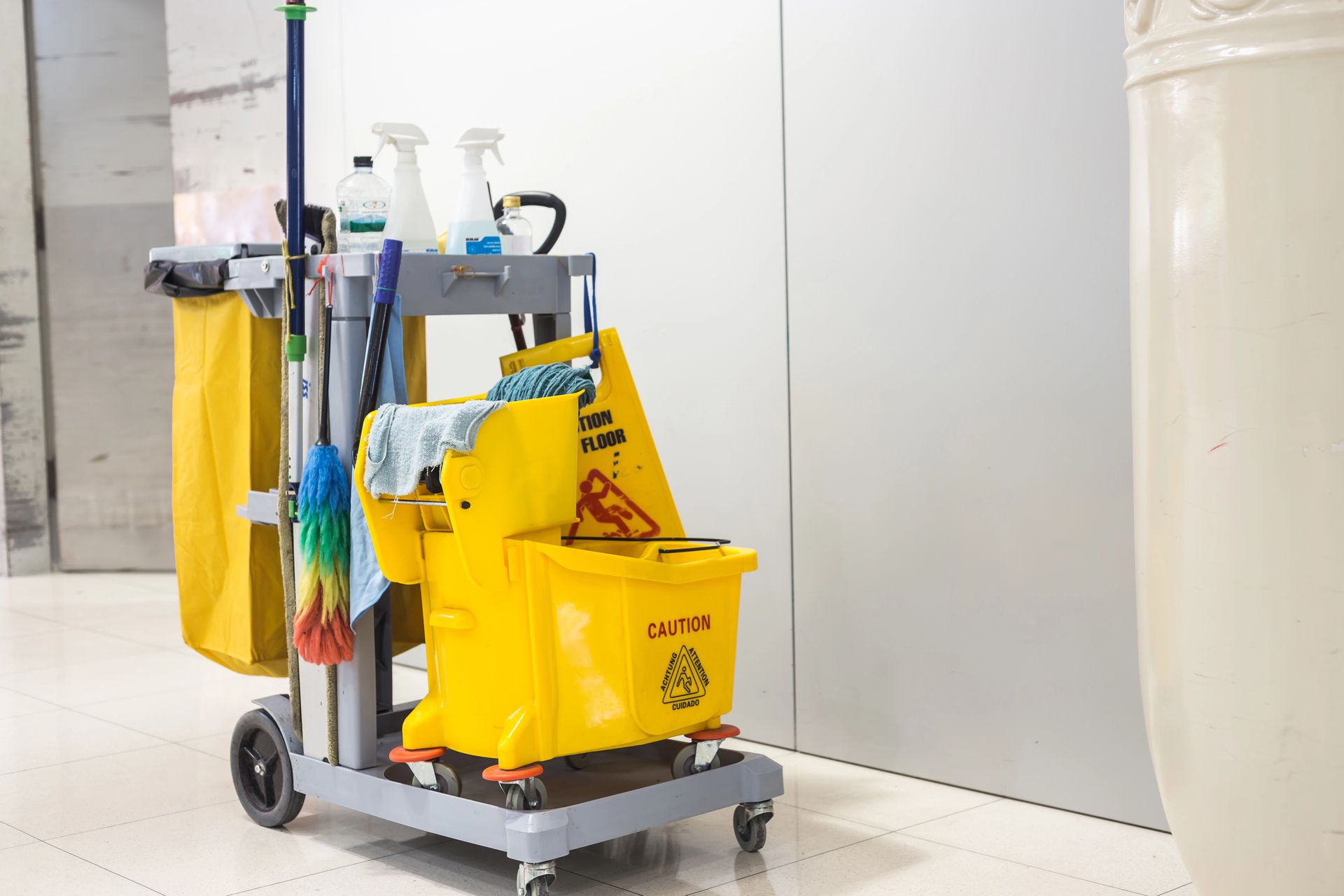 Janitorial cleaning cart with yellow trash bags and supplies in a hallway
