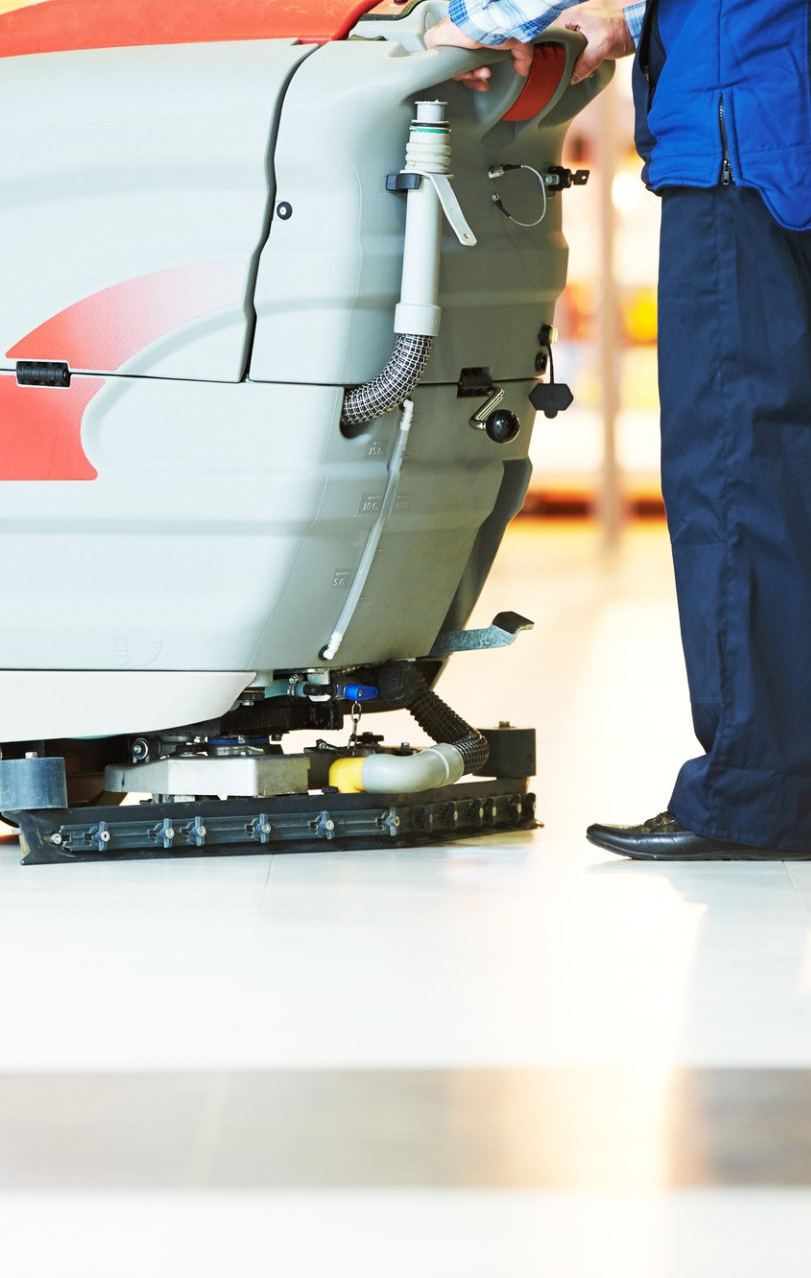 A man is standing next to a machine that is cleaning the floor.