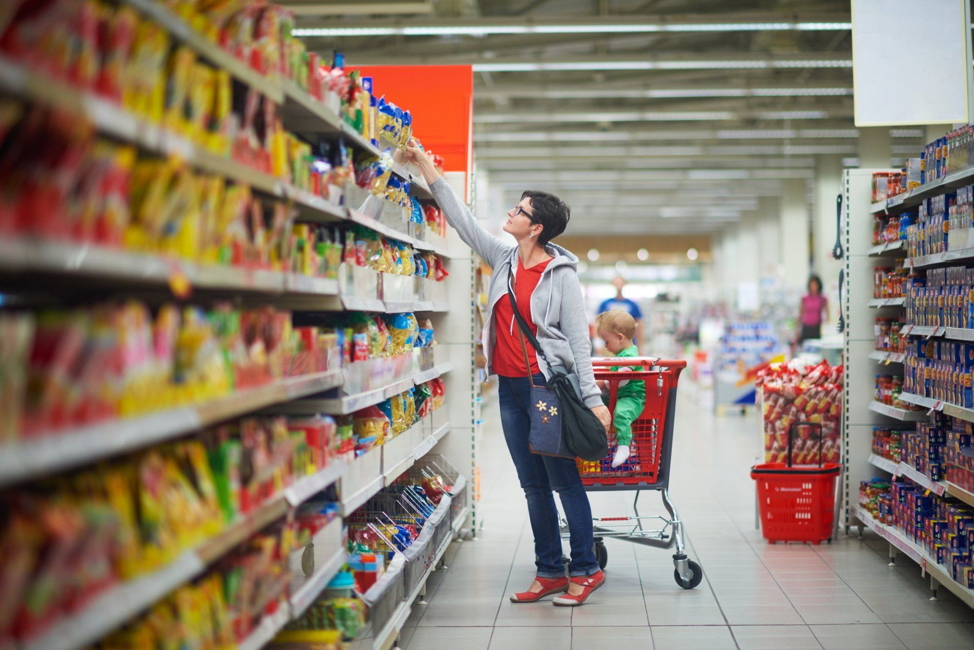 A woman is shopping in a grocery store with a shopping cart.