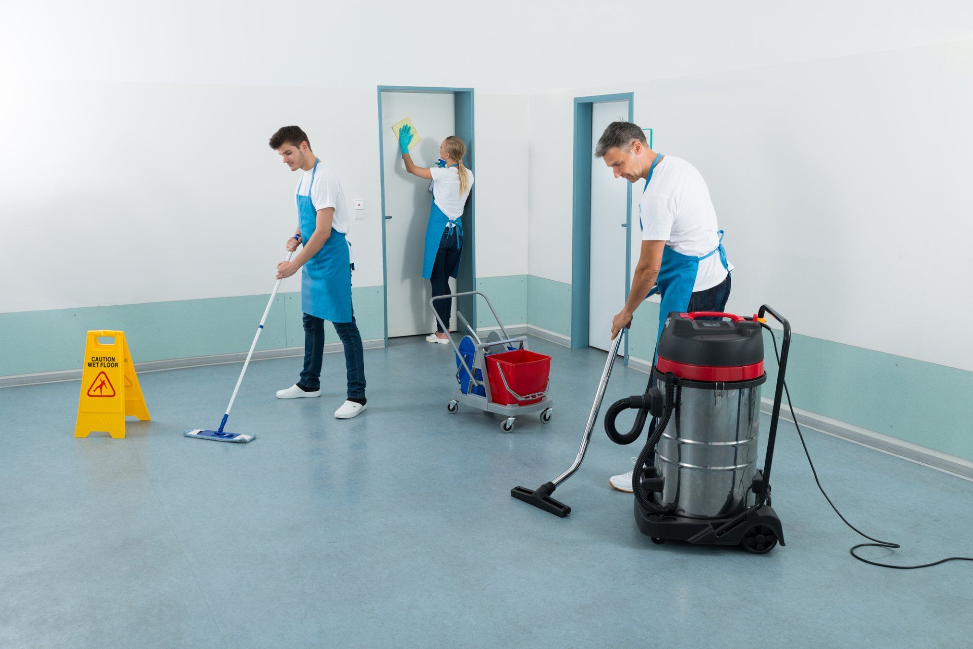 A group of people are cleaning a room with mop and vacuum cleaners.