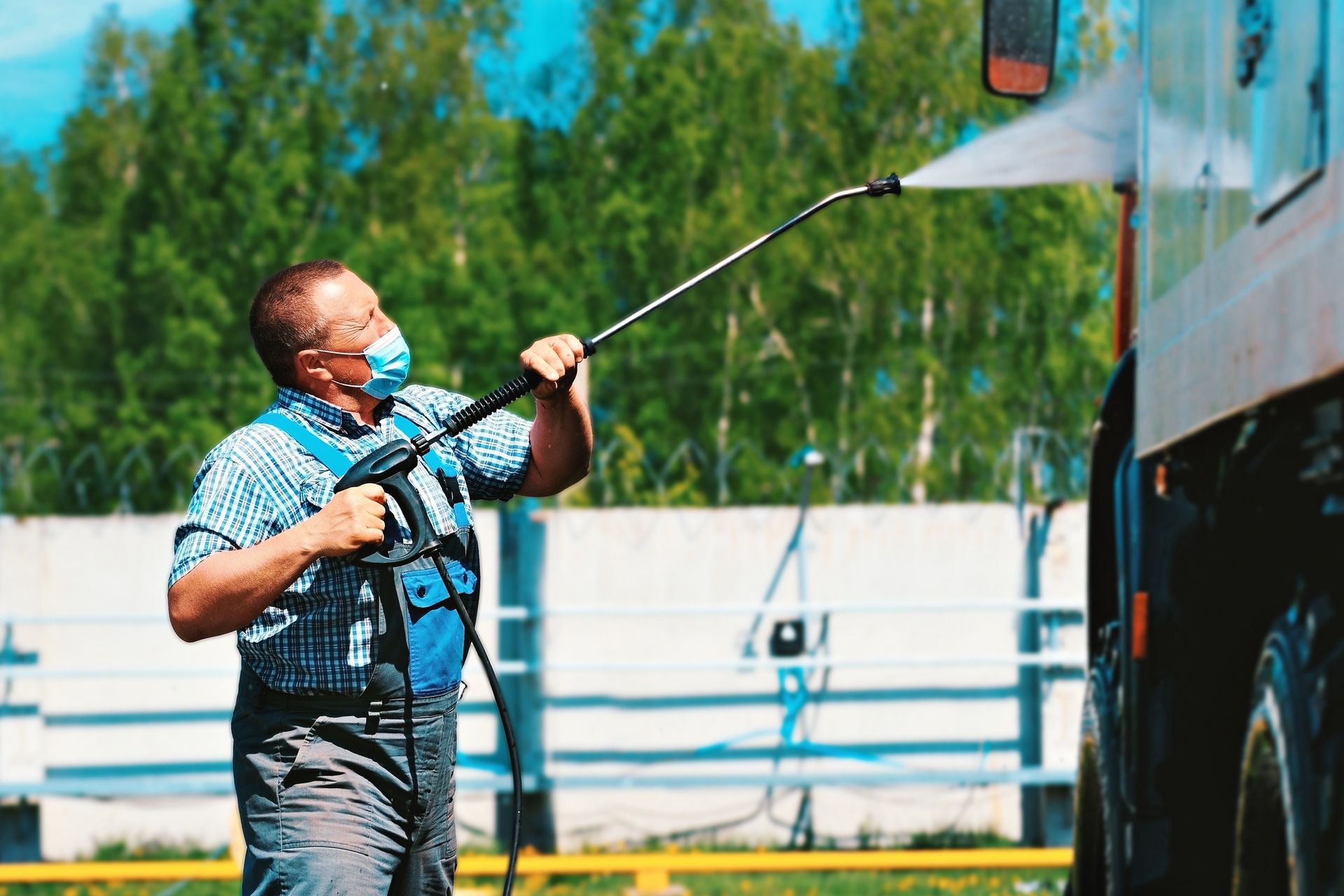 Man wearing a mask pressure washing a truck outside.
