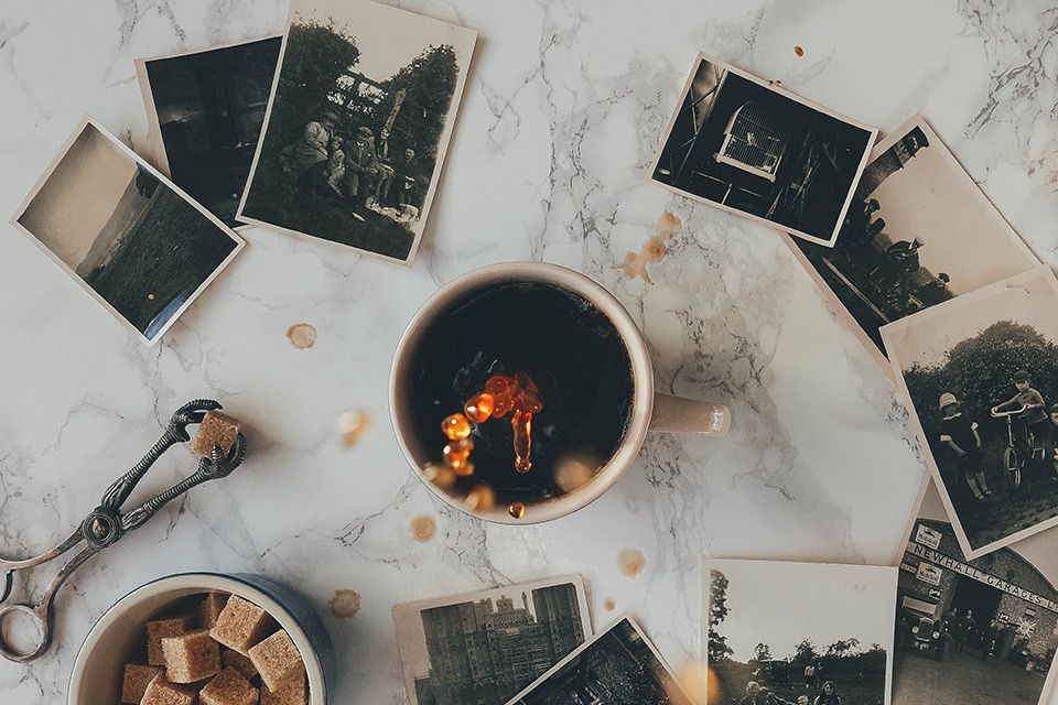 A cup of coffee is surrounded by old photographs on a marble table.