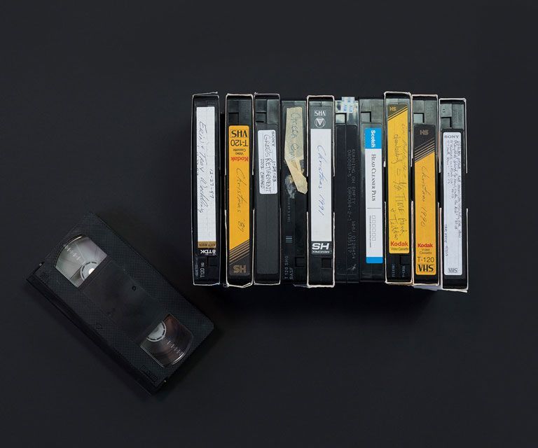A pile of 2 vhs tapes on a wooden white surfaces. The top vhs tape has flowers on top of it