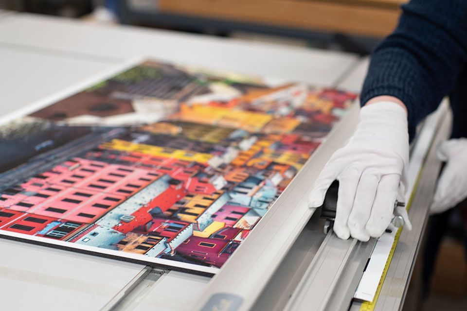 A color print of a European town being mounted and cut for wall decor.