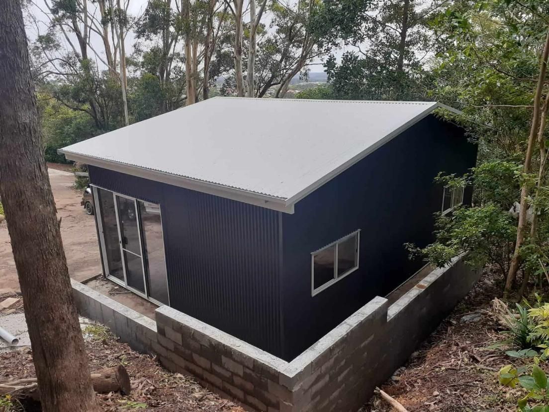 A Small Black Building With a White Roof is Surrounded by Trees — Hastings Valley Sheds in Wauchope, NSW