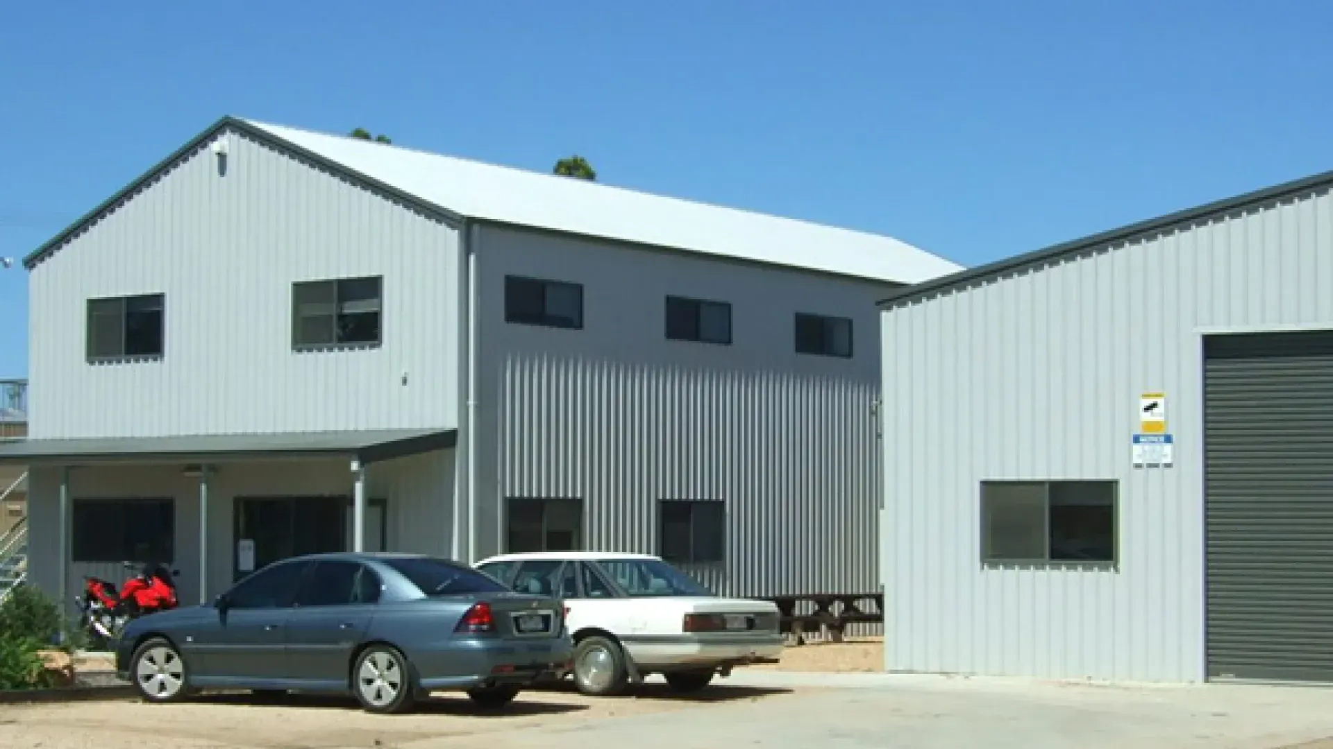 Two Cars Are Parked in Front of a Large Building — Hastings Valley Sheds in Kempsey, NSW