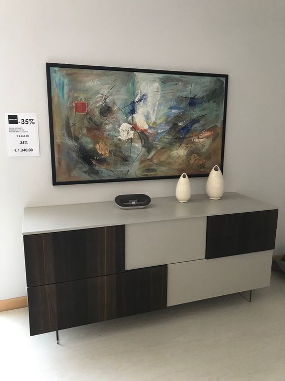 Credenza moderna con opere d'arte, due vasi bianchi e un oggetto nero sopra, contro una parete bianca.