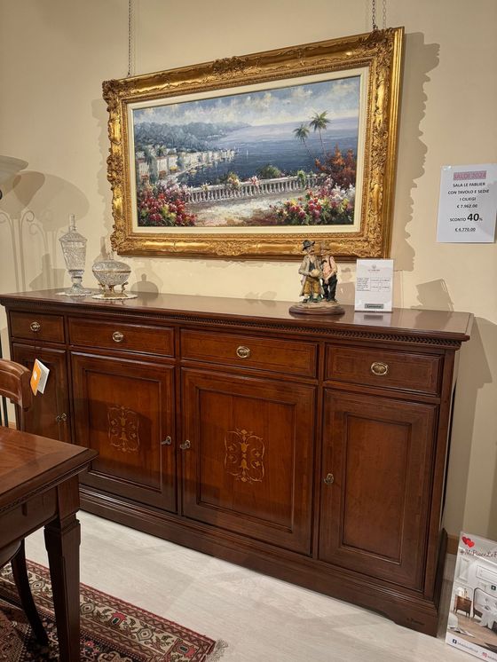 Buffet in legno con dipinto incorniciato sopra; due oggetti di cristallo e una statuina sopra.
