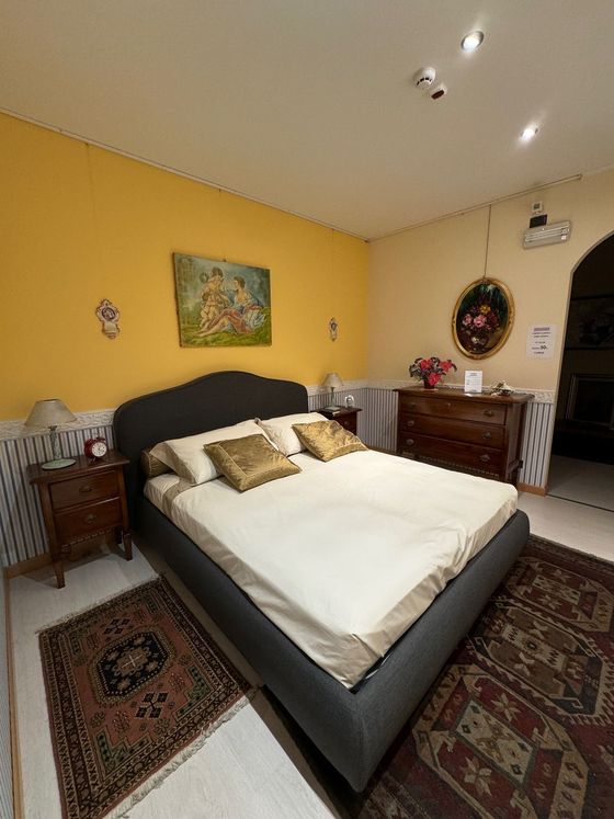 Camera da letto con letto grigio, pareti gialle, mobili antichi e tappeti a fantasia.