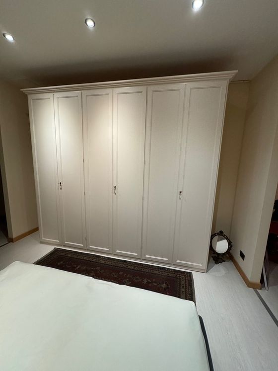 Grande armadio bianco a muro in una camera da letto, sopra un tappeto scuro e accanto a un letto.