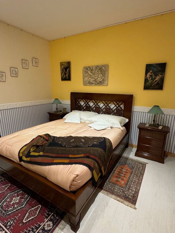 Camera da letto con letto in legno, parete gialla, piccoli tappeti e opere d'arte.
