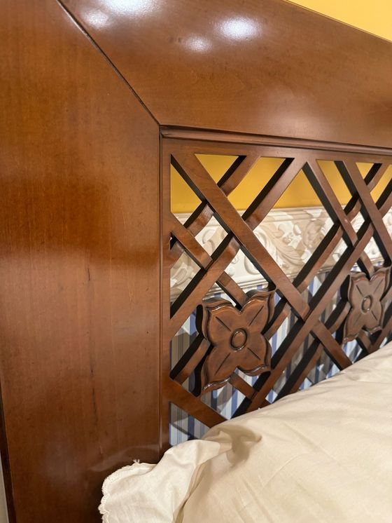Testiera del letto in legno con traliccio e dettagli floreali, sopra un cuscino bianco.