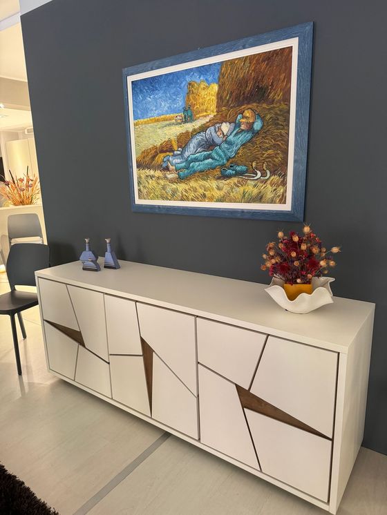 Credenza bianca con motivi geometrici, sotto un quadro. Decorata con vasi e una composizione floreale.