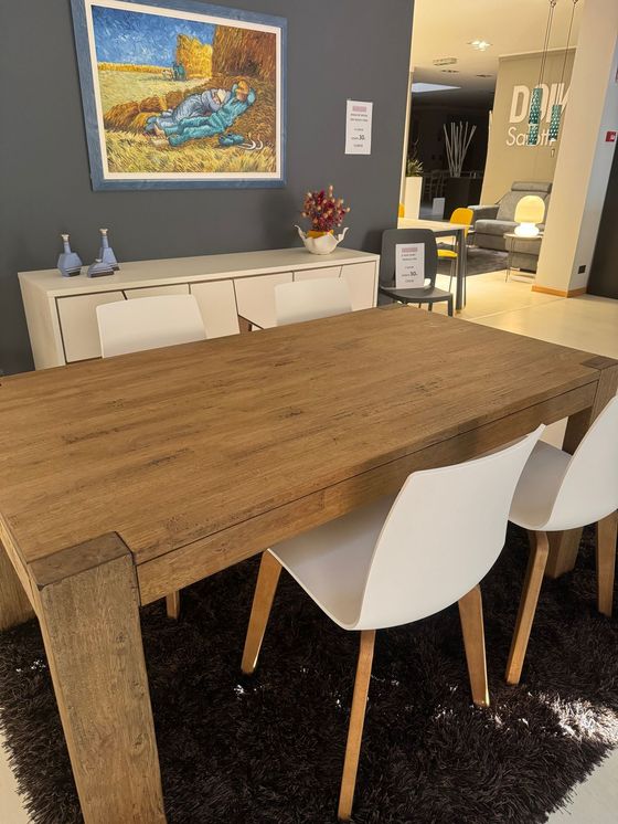 Tavolo da pranzo in legno con sedie bianche su un tappeto nero, in uno showroom.