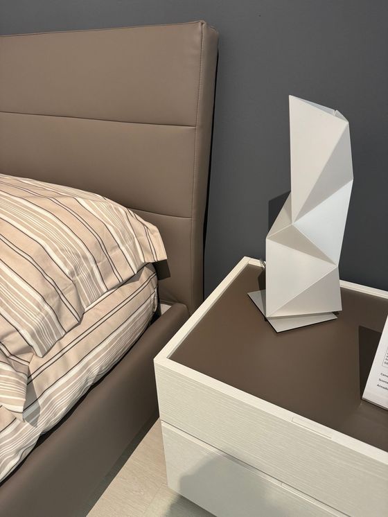 Letto con testiera imbottita e comodino con lampada geometrica.