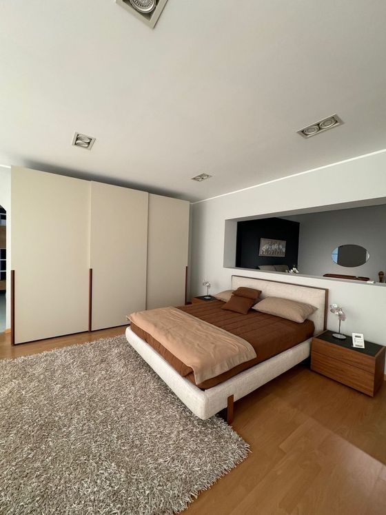 Camera da letto con armadio bianco, letto con lenzuola marroni e tappeto grigio.