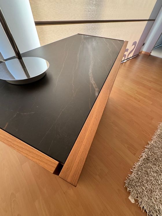Tavolino da caffè con piano in marmo nero e struttura in legno, posizionato su un pavimento in legno massello.