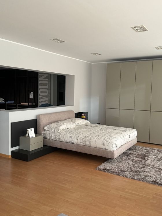 Camera da letto con letto, biancheria da letto a fantasia, comodino, tappeto grigio e ampio armadio.